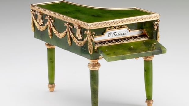 This miniature grand piano in Louis XVI style was made by Mikhail Perkhin. It’s made of nephrite with mounts of red and green gold, and the keyboard is opaque black and white enamel. Foliate swag mounts are around the edge and the top is hinged; 2” x 2.8” x 2”. Judging by her acquisitions, Queen Mary was particularly fond of Fabergé’s miniature objets de fantasie, which include several examples of miniature furniture in the form of bonbonnières. These objects afforded the craftsman the opportunity to demonstrate skill in applying specialist techniques to replicate the real materials of the full-scale object. This miniature piano of Siberian nephrite is carved and polished to resemble ebonized wood. The lid opens for use as a bonbonnière and the front drops down to reveal the keyboard in gold and enamel, inscribed “C. Fabergé.” The piano belonged originally to Tsarina Alexandra Feodorovna and is also seen in one of the display cases in photographs of the exhibition of Fabergé held in St. Petersburg in 1902. Queen Mary acquired it sometime between 1922-1931.