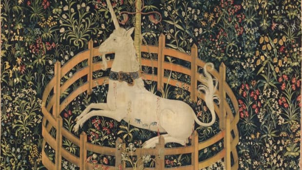 Tapestry 7: The Unicorn in Captivity. This tapestry shows the unicorn alive and well, and entirely tamed. He is fenced in and chained to a tree, but the chain is less than secure and the fence is low enough to leap over. He has submitted to his captivity. The red stains on his flank, according to the Met, “do not appear to be blood, as there are no visible wounds like those in the hunting series; rather, they represent juice dripping from bursting pomegranates” — a medieval symbol of marriage and fertility. Many of the other plants represented here, such as wild orchid and thistle, echo this theme of marriage and procreation: they were acclaimed in the Middle Ages as fertility aids for both men and women.
