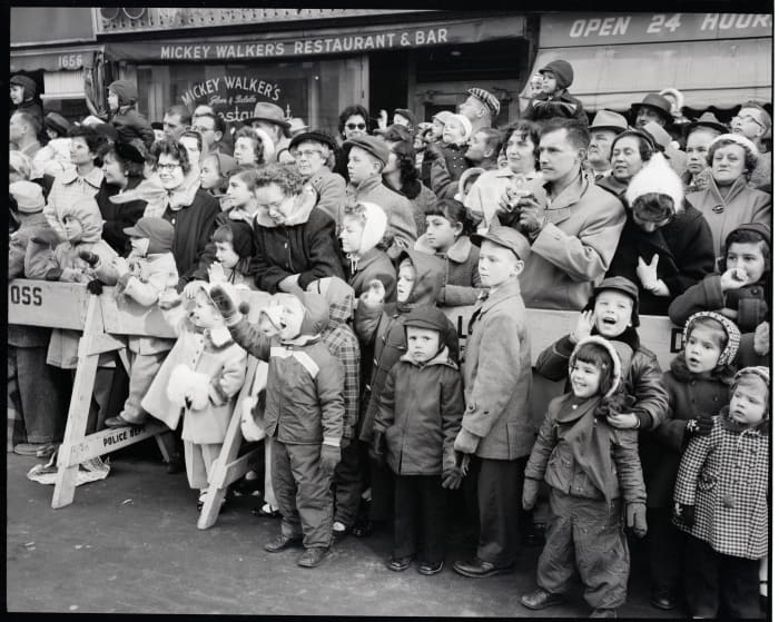 The crowd at the 1956 parade behind a police barricade, with children watching in the front.