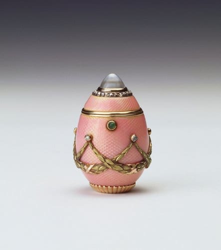 This egg-shaped box of two-color gold and pink guilloché enamel was made by Carl Fabergé, c. 1900; 1-1/2” x 1”. The lid is set with a domed rock crystal with a surround of rose diamonds and the body is hung with crossed yellow gold laurel swags suspended from rose diamonds. The egg has a cabochon emerald thumb piece and a gadrooned base. Fabergé produced boxes, pendants and even cups in the form of eggs and there are numerous examples of these objects in the Royal Collection.