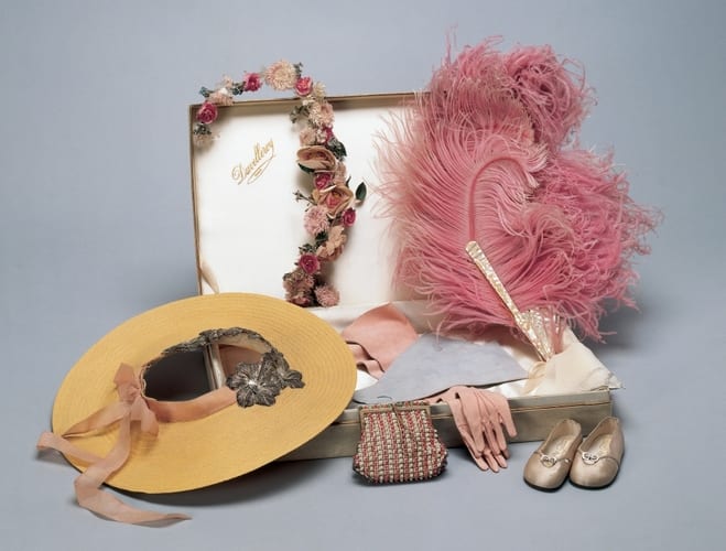 This group of tiny fashion accessories includes a pair of pale pink silk slippers with two silver buttons on the front of the shoe joined with a silver link and cut-out moons, and leather soles stamped with crosses. These were a state gift to Princess Elizabeth and Princess Margaret Rose from the children of France during a state visit by the king and queen in 1938.