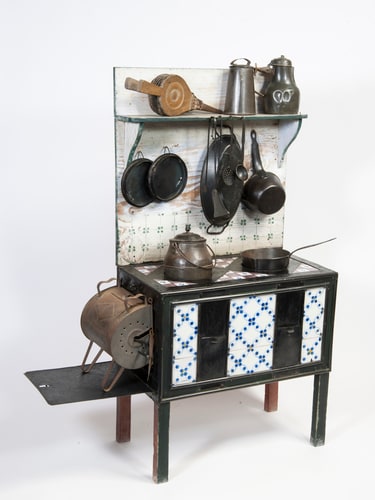 This model kitchen range from the 19th century is made of wood, iron, tin and enamel and features a painted wood back, purple and blue tiles and a back shelf to support the 13 miniature accessories and utensils.