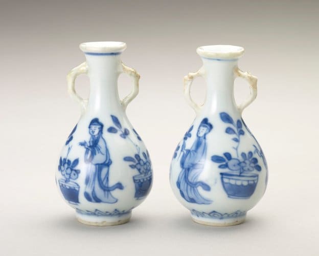 Two blue-and-white miniature porcelain bottles painted in underglaze blue, Jingdezhen (Jiangxi Province, China), 1690-1700, about 3” h. Each pear-shaped, with tapering neck and spreading lip, the sides have a pair of animal-headed loop handles picked out in brown glaze. Painted in panels round the sides are three women tending flowers in pots, with a petal border below.