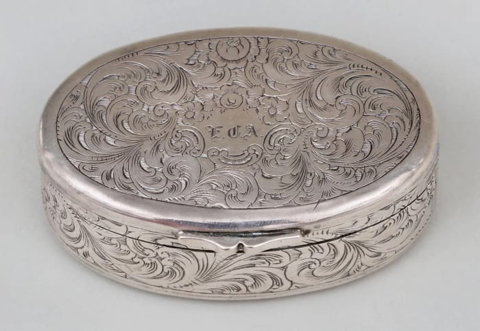 Coin silver oval nutmeg grater, C. Stewart, circa 1845-55, hinged lid with an applied finger tab, body engraved with arabesque scrolls, 1” h, 2-5/8” w, 1-7/8” d; $3,300.