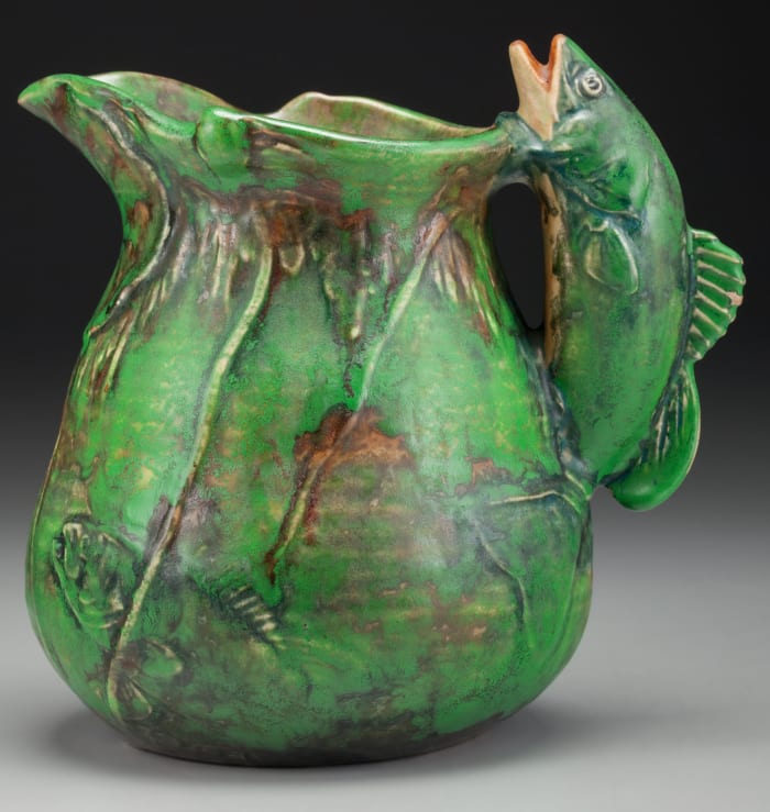 Coppertone ceramic pitcher with molded and incised lily pad and fish decoration to the body and a molded fish-form handle, Zanesville, Ohio, circa 1925, 7-1/2” h; $525.