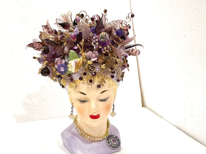 Napco hand-painted amethyst lady head vase, 1960, signed and numbered, hand painted, original drop “faux” pearl earrings and necklace,  and prong-set lavender rhinestone brooch on a lavender dress. Showcases over 80 handmade flowers, over 180 hand-set Swarovski crystals, 40 hand-torched flowers and leaves and over 30 hand-made brass fancy, swirled pins with rhinestones inset by the seller. Without flowers, 5-1/4” h, with flowers, 8-1/2” h; $320.
