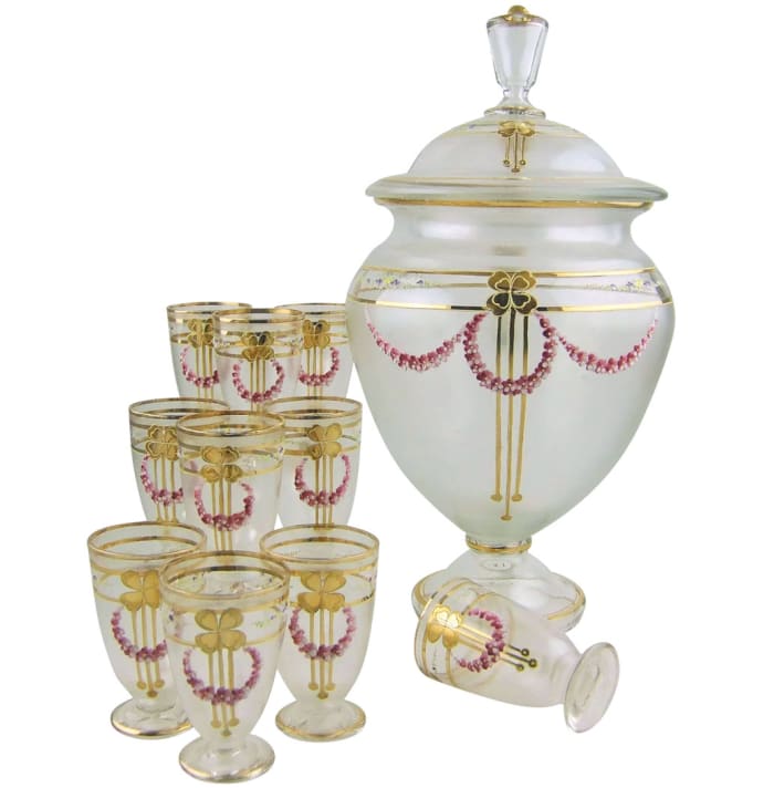 A circa 1900 Art Nouveau Jugendstil glass punch set with an elegant lidded, pedestal-foot punch bowl and ten handled, pedestal foot cups. The lightly iridescent, frosted and colorless glass is decorated with textured polychrome flower swags, gold borders and gold four-leaf clovers with stylized stems with drops: $299.
