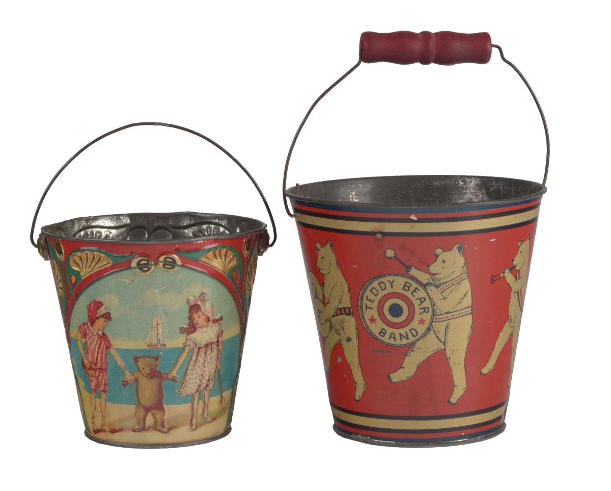 Lot of two early tin sand pails with teddy bear themes including an embossed German one of children playing with a teddy bear on the beach on one side, a sand fort on the other, and an embossed lobster on the bottom, 6” h; and a Teddy Bear Band with an embossed eagle on the bottom, 9 -1/2” h; $540.