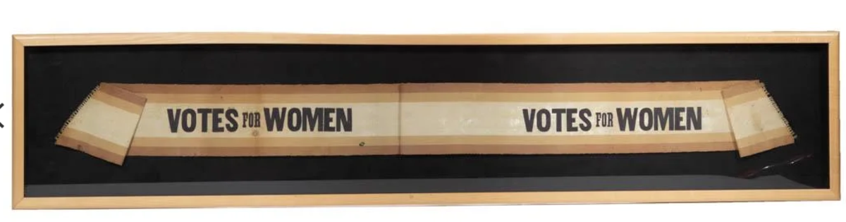 A suffrage parade sash of printed grosgrain fabric bearing the slogan,  “Votes for Women,” in purple/black block letters within a two-tone border, circa 1910, 10” x 47”, $2,300.