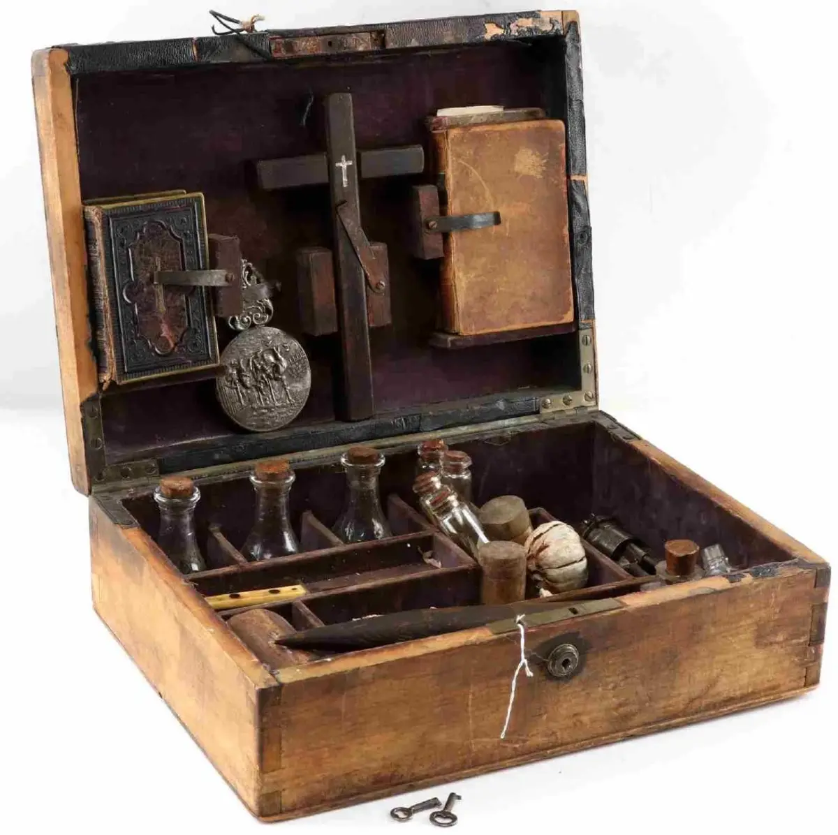 Applied Auctions sold this kit in 2019 for $2,600. The lid holds a book of psalms and proverbs in German a small hand-held mirror, cross inscribed with another cross in the middle, glass bottles, small knife, four glass vials, two small wooden jars, two candles and garlic, a mallet, and stakes. Bottles hold nails, garlic, holy water, matches and other unidentified items.