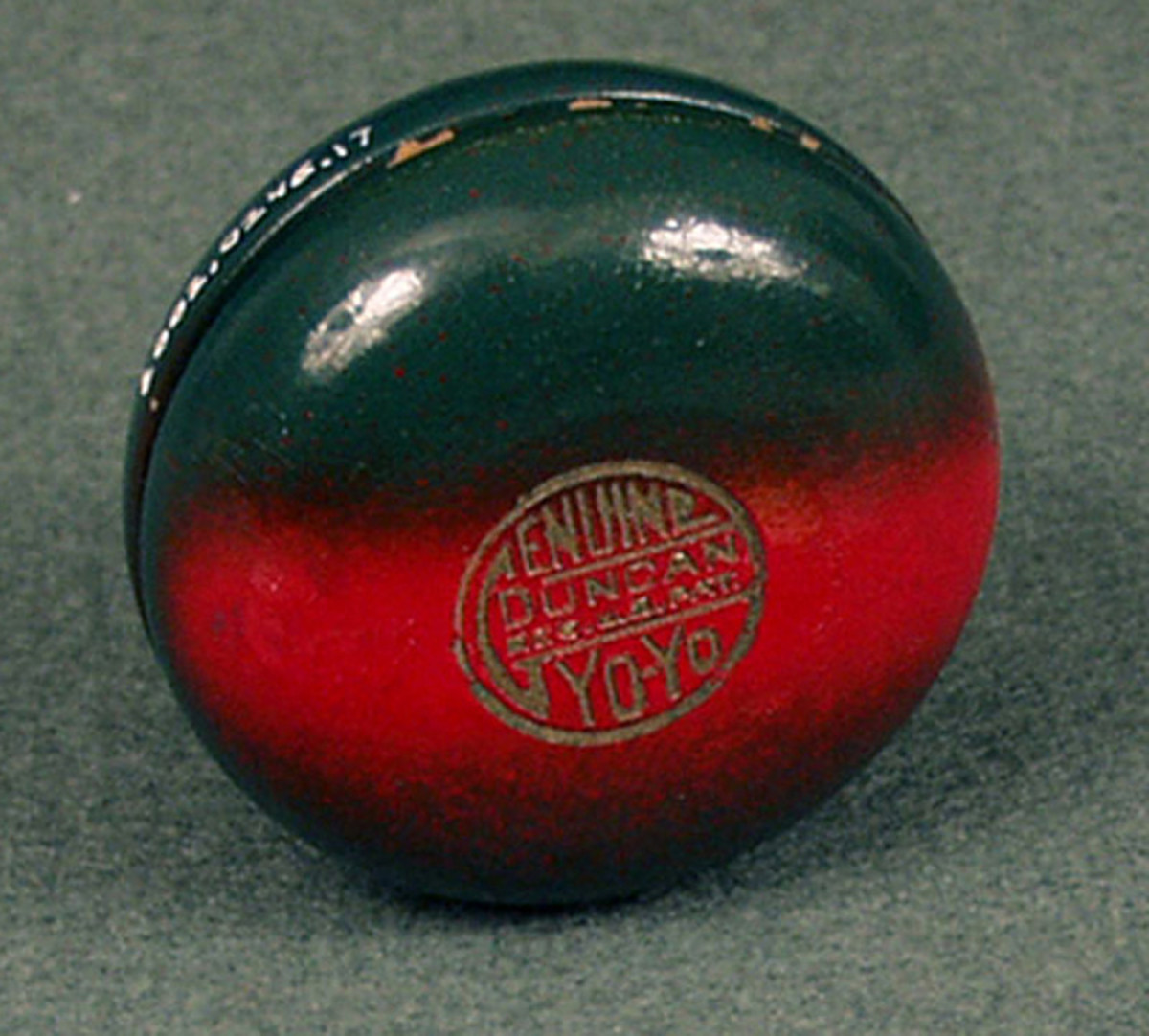 A wooden yo-yo made by the Duncan Toys Company, 1930s. It has a green design with a broad red stripe. The seal reads “Genuine Duncan Yo-Yo, Reg. US Pat.” This is an early version of the Duncan Genuine Yo-Yo, produced soon after Donald Duncan bought the trademark term “yo-yo” from inventor Pedro Flores, and the seal is reminiscent of the one used by Flores.