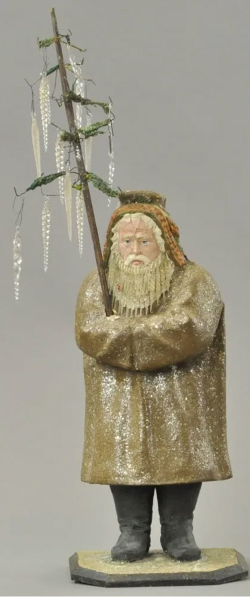 Large German Belsnickle candy container with glass beard, composition figure wearing long brown robe flecked with mica, golden beads around his hood, holding a lichen moss tree in arms and standing on mica-flecked wood base. This Belsnickle has a kind expression, rather than the usual stern one; 16" h. Sold for $22,500 in 2016.