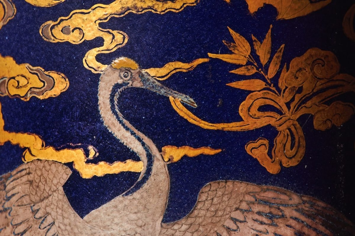 One of the cranes on the vase holding a symbol of Daoism.