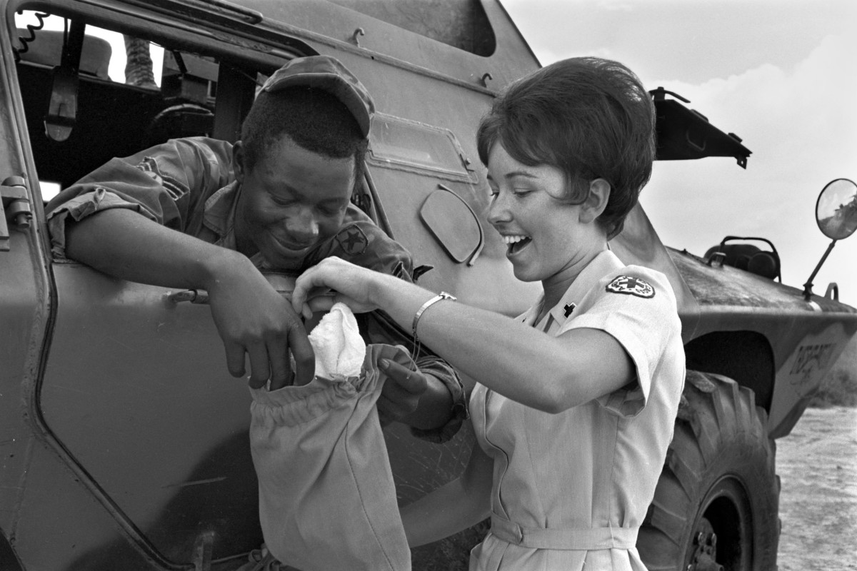 At Tan Son Nhut Air Base, Vietnam, in 1970, Red Cross worker Christine Foerster, 21, of Orlando, Florida, and Sgt. Thomas L. Micka, of Vicksburg, Mississippi, investigate the contents of his ditty bag. Sgt. Micka was on guard along the Tan Son Nhut air base perimeter in an armored personnel carrier.