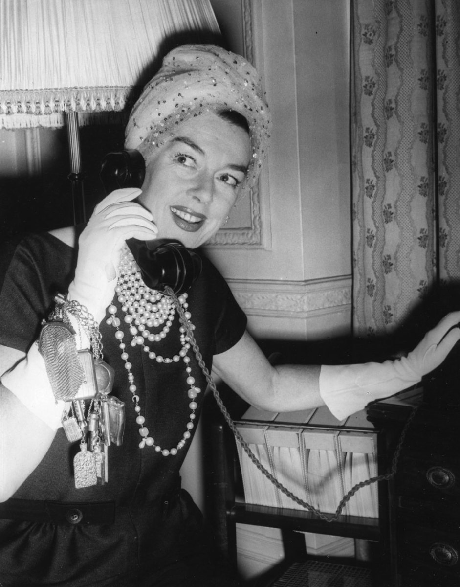 Actress Rosalind Russell wears her famous gold chatelaine on her wrist, made from presents given to her by various friends, while making a call in her London hotel room in 1958.
